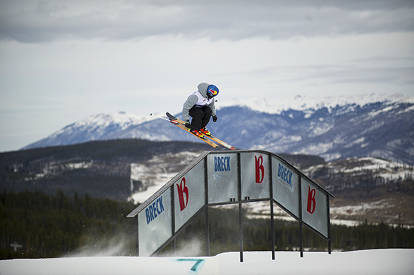 A skier catching air in the foreground with the mountains in the background.
