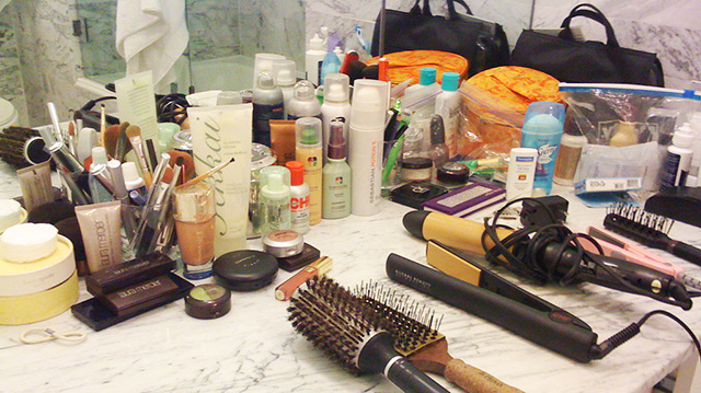 Multiple toiletry items, beauty supply items and makeup fill a bathroom counter.